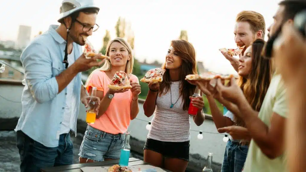 A group of friends enjoying pizza and drinks at an outdoor gathering.