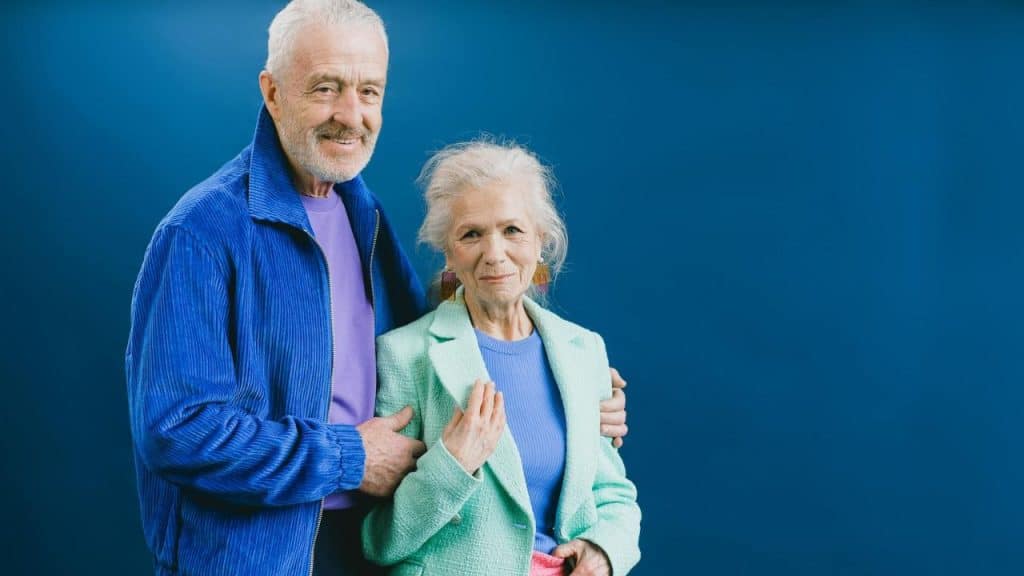 An older man in a blue corduroy jacket stands with an older woman in a mint blazer.
