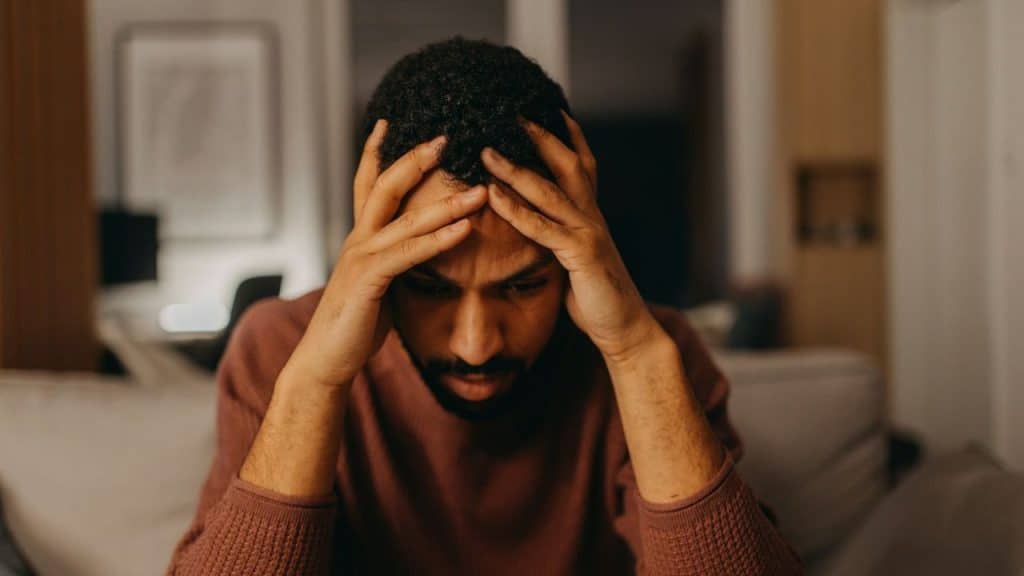 A man sits indoors with both hands held against the sides of his head.