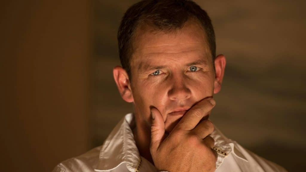 A man in a white collared shirt rests his chin on his hand and looks forward.