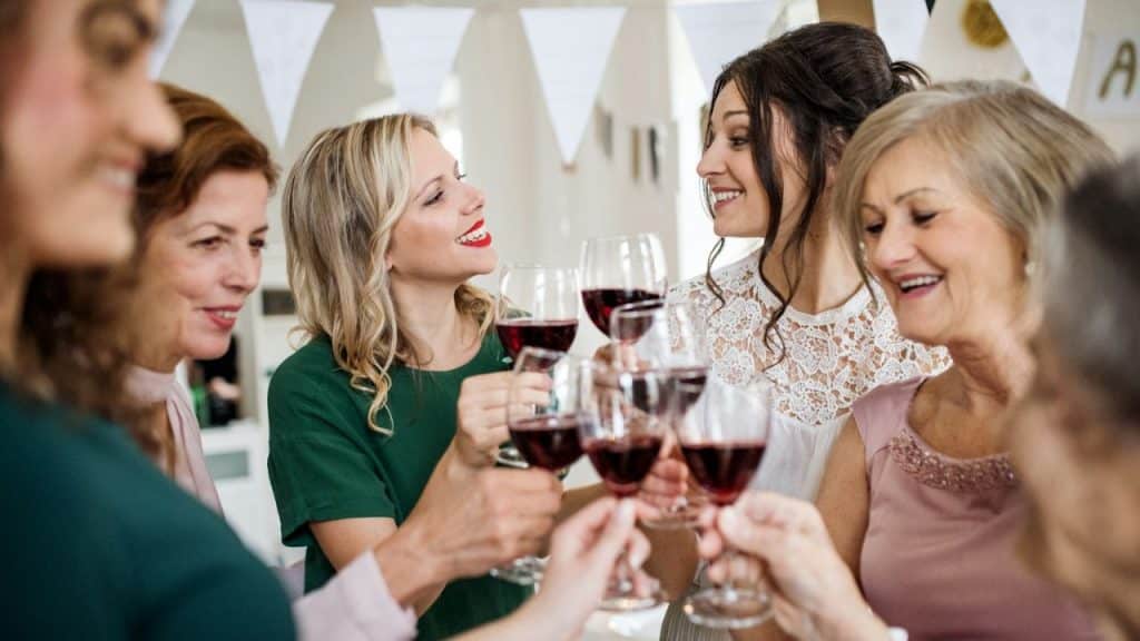 A group of women smile and toast together with glasses of red wine.