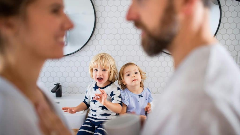 A toddler and a preschooler sitting on a bathroom counter between their parents.