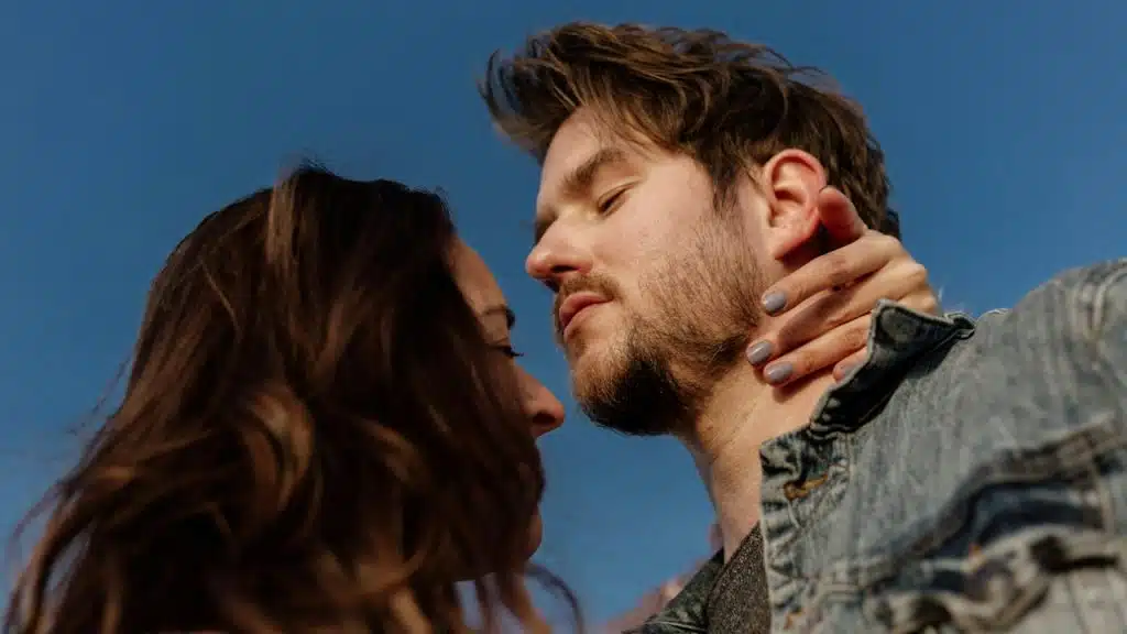 A lightly bearded man staring at a woman while she holds his neck with her hand. 