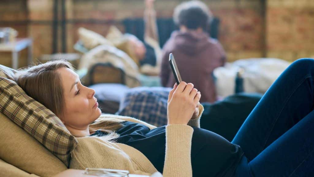 A pregnant woman lying down looking at her phone.