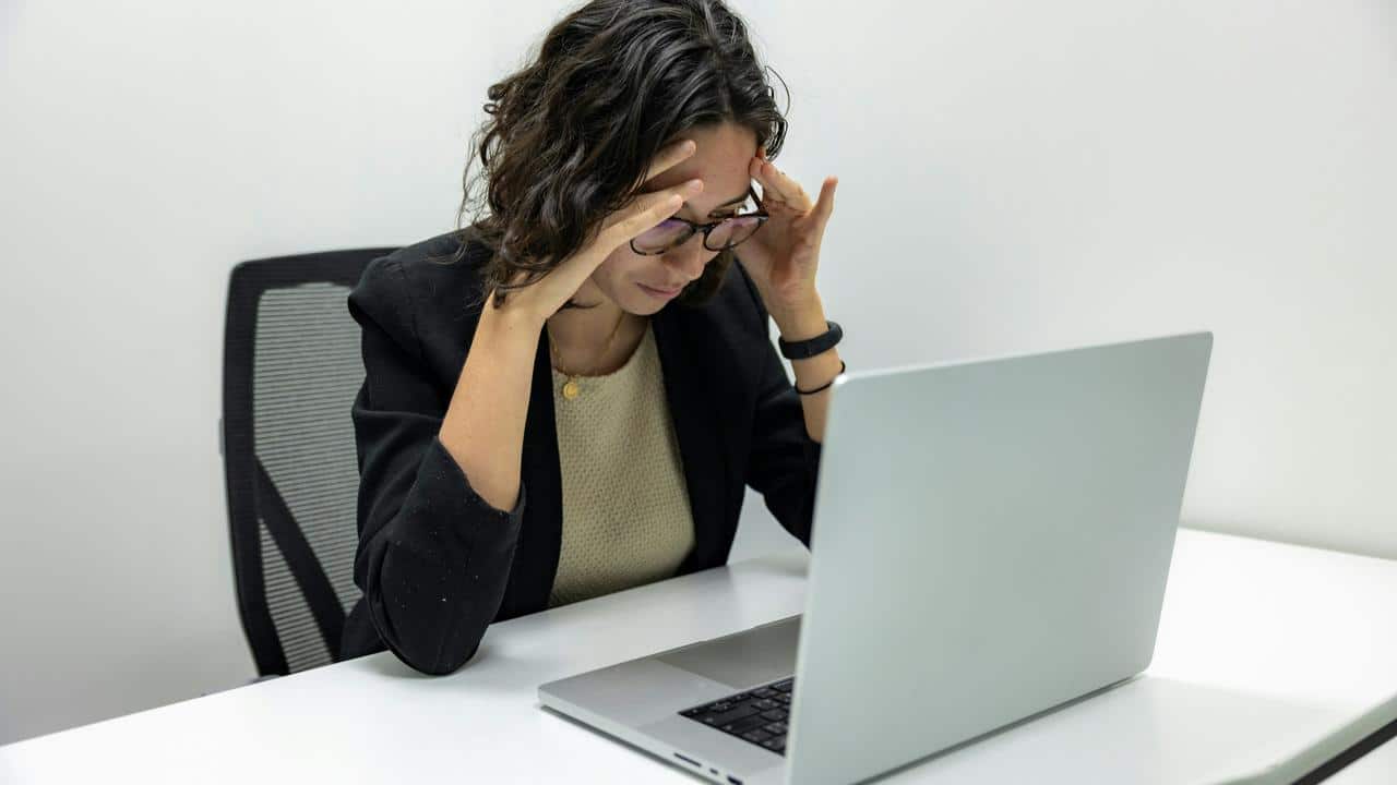 A woman holding her head in frustration while working on a laptop.