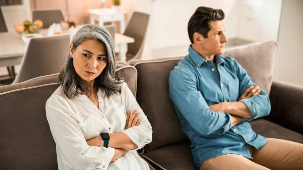 A man and woman sit on a sofa with arms crossed, looking away.