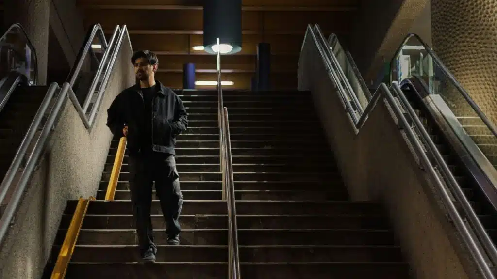 A man in a dark jacket walks down a wide concrete staircase in a dimly lit area.