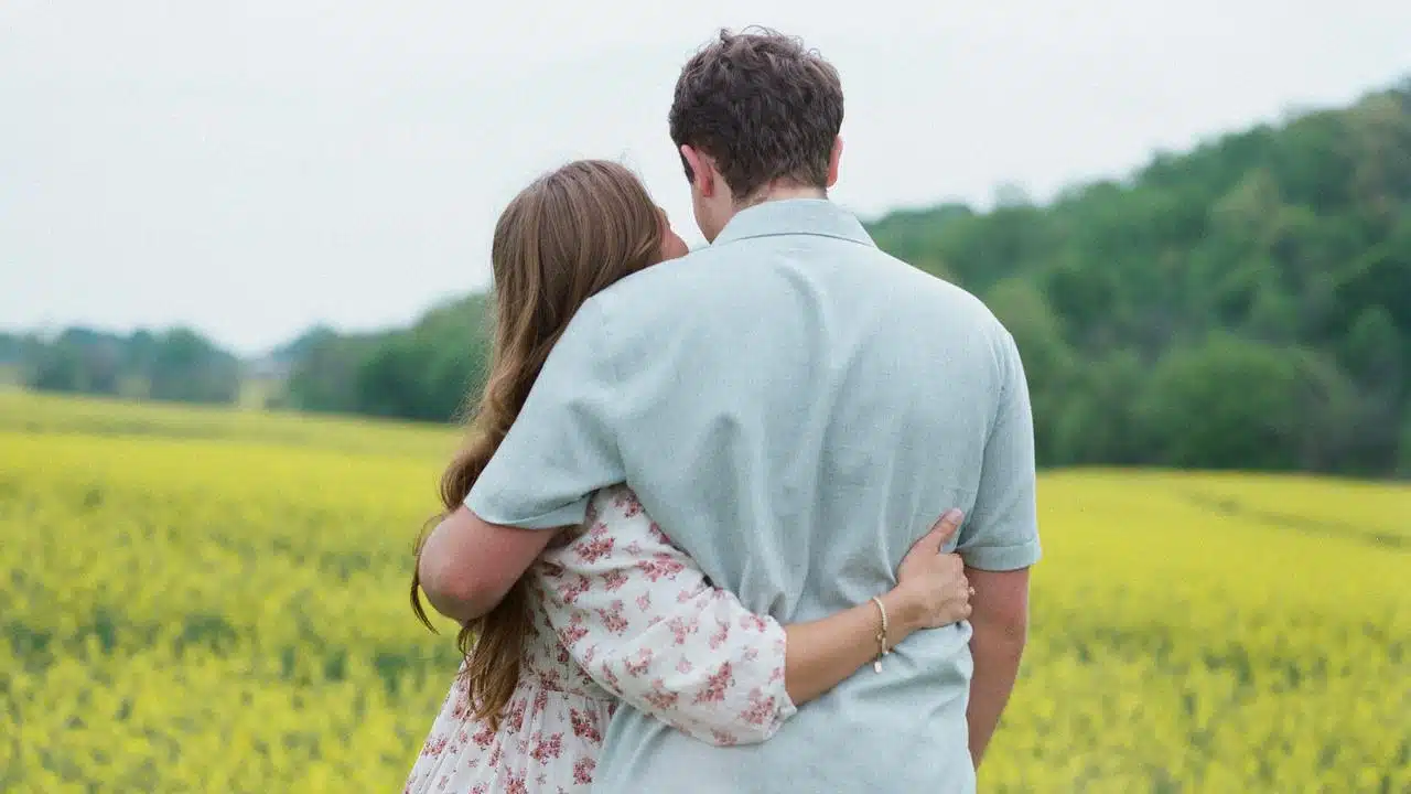 A couple embracing while looking out over a field of yellow flowers.