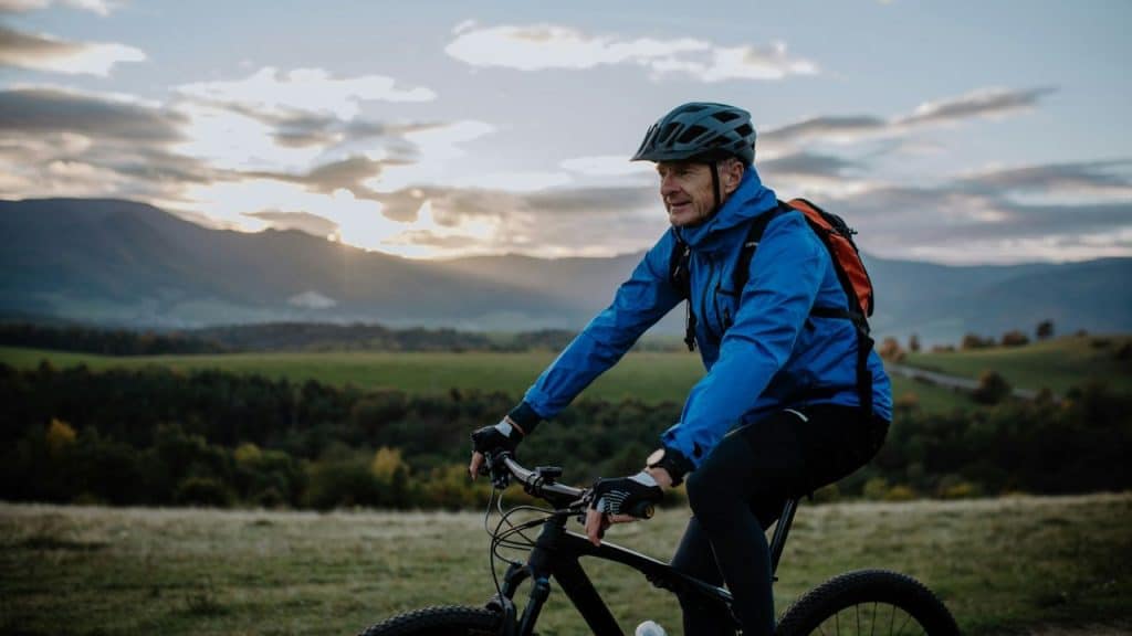 A man wearing a helmet and blue jacket rides a bicycle through a rural landscape.