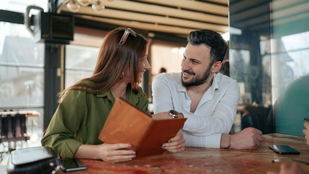 A smiling man and woman look at a brown menu together at a table.