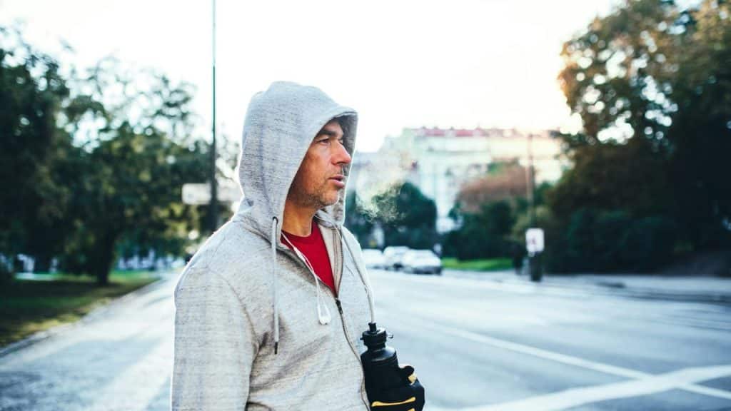 A man in a gray hoodie holding a water bottle outdoors.