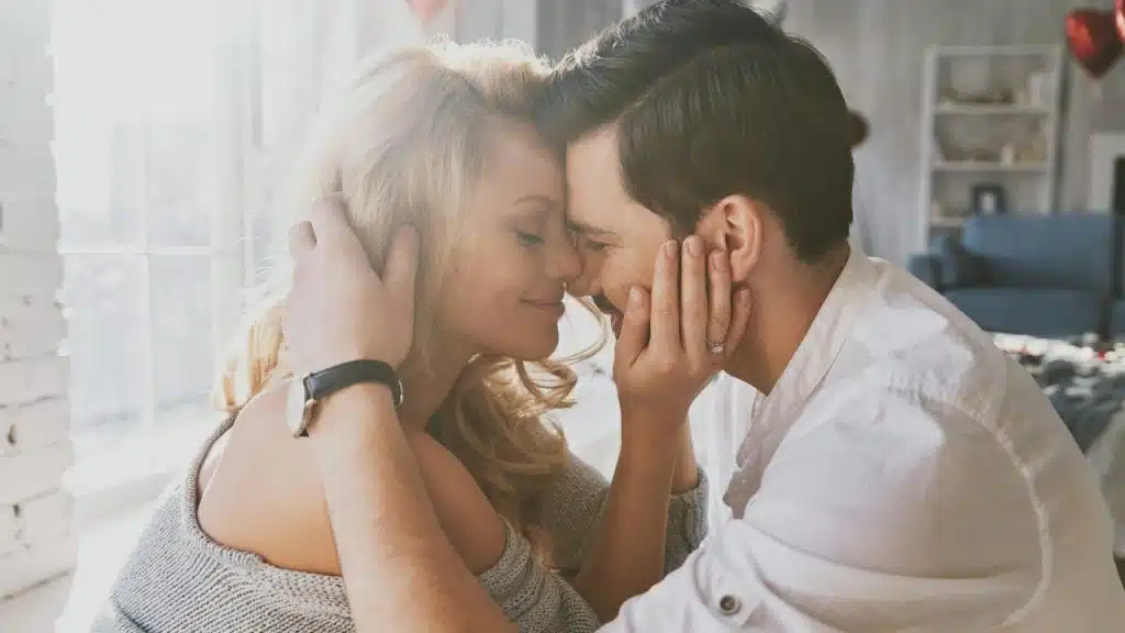 A man holds a woman's face with both hands while they touch foreheads and smile.