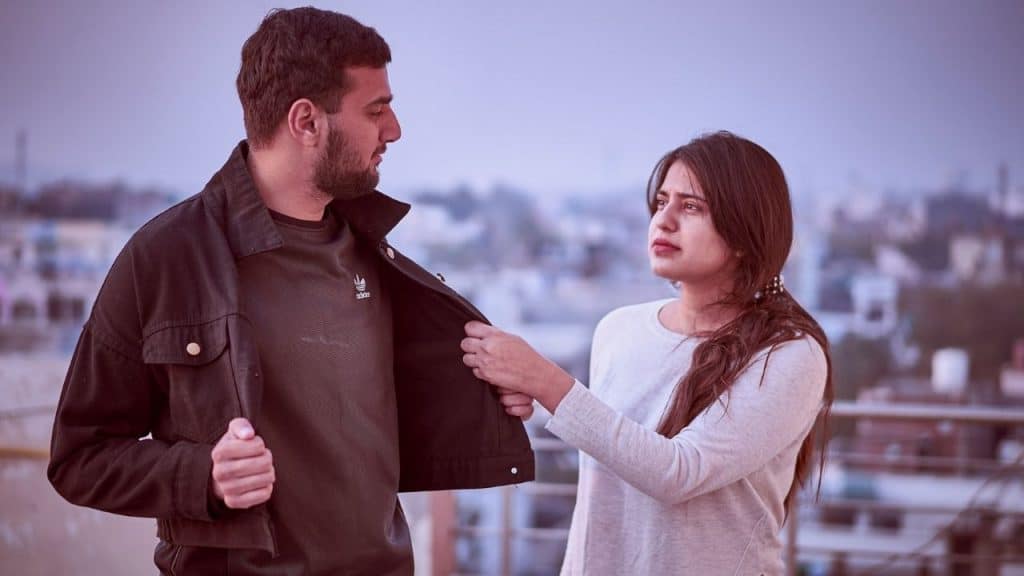A woman holds the edge of a man’s open jacket as they look at each other.