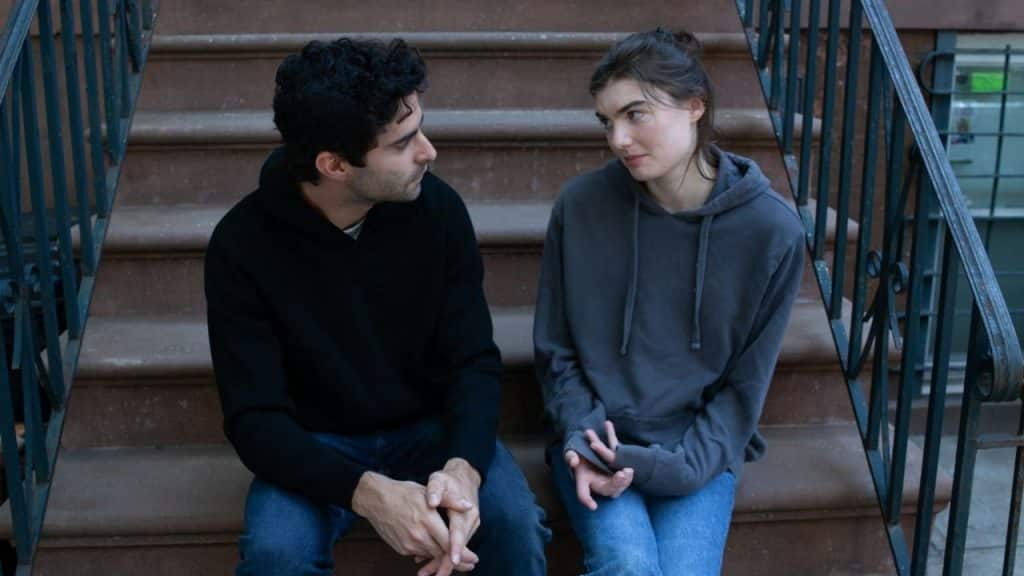 A man and woman in hoodies sit on outdoor stone steps and look at each other.