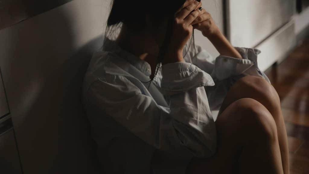 A person sitting on the floor by a wall with their head in their hands.