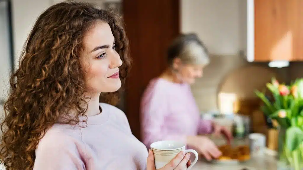 A person holding a mug and smiling in a kitchen.
