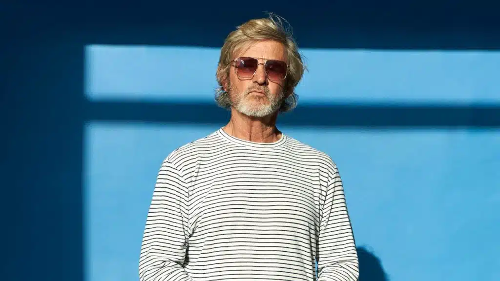 A middle-aged man standing in front of a blue wall.