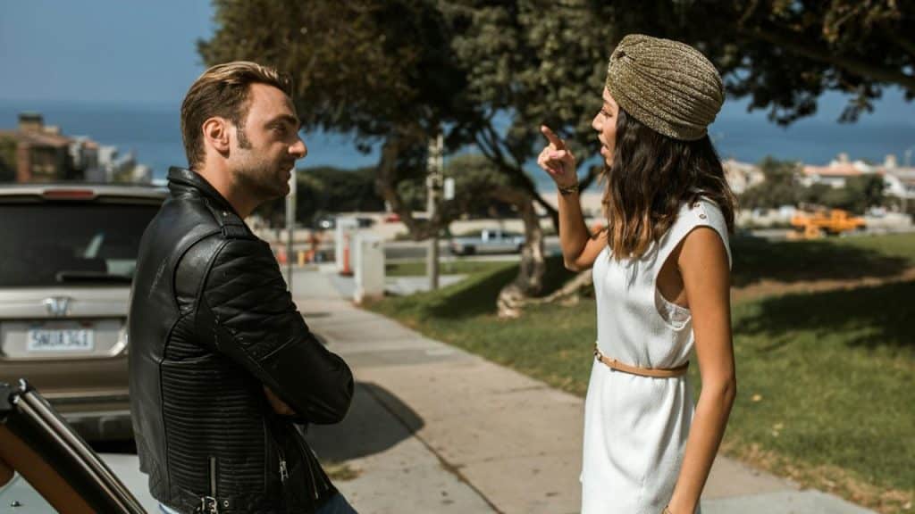 A woman in a gold turban points her finger while talking to a man outside.
