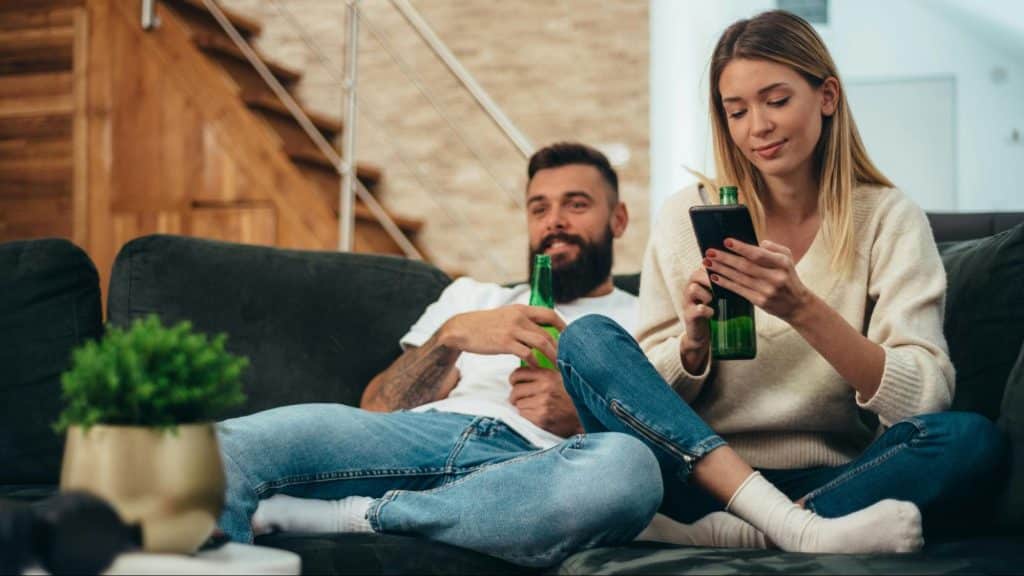 A man and woman at the living room having a beer