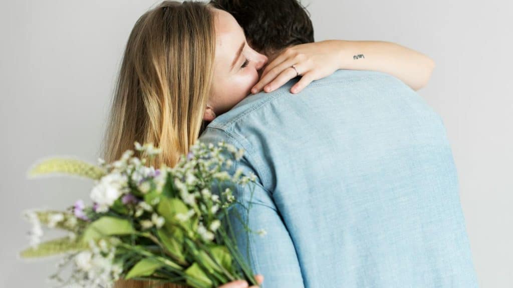 A couple embracing closely, with the woman holding a bouquet of flowers.