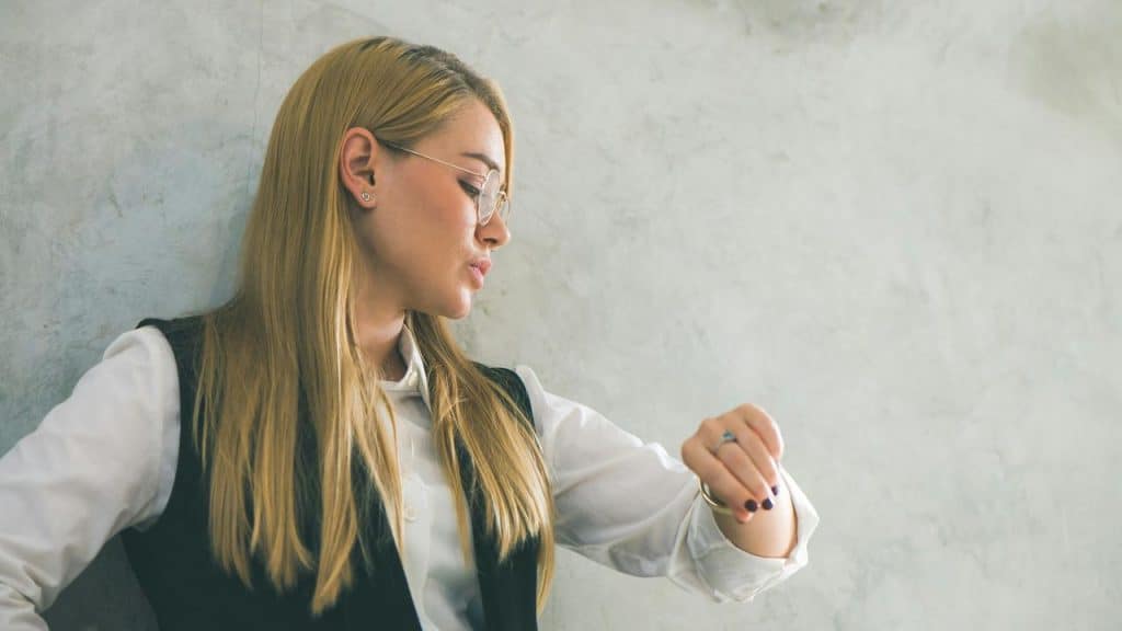 A woman wearing glasses looking at her wristwatch.