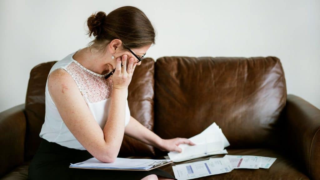 A woman sits on a brown leather sofa looking down at several scattered paper documents.