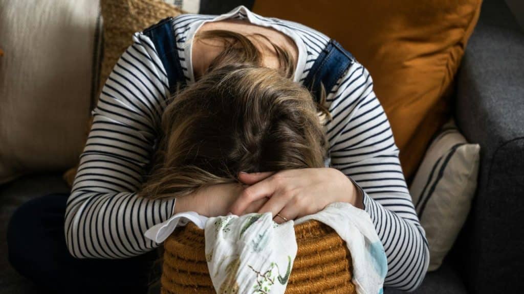 A person in a striped shirt rests their head on their arms over a woven basket.