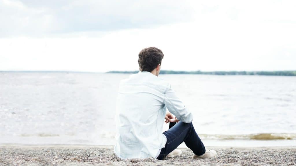 A man sitting on a beach and looking over the ocean.