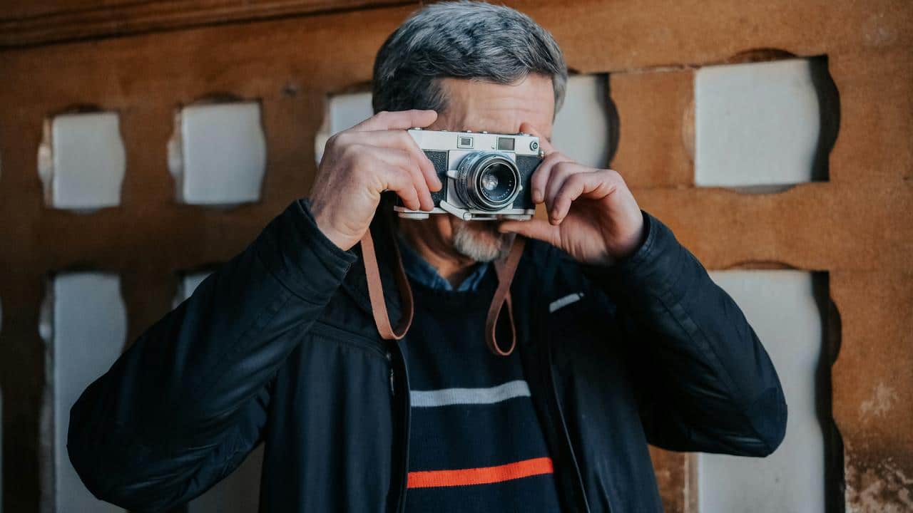 A senior man holding a camera and taking photographs.