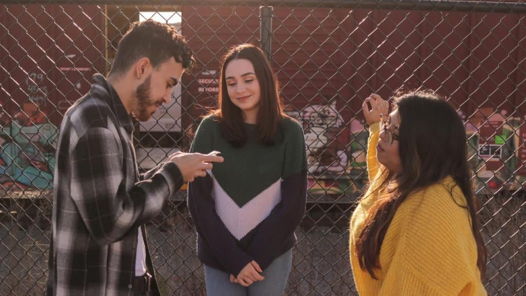 A small group of friends standing and talking near a chain-link fence.
