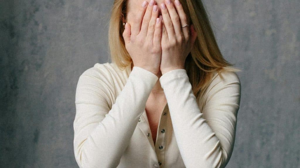 A woman covering her face with both hands against a plain background.
