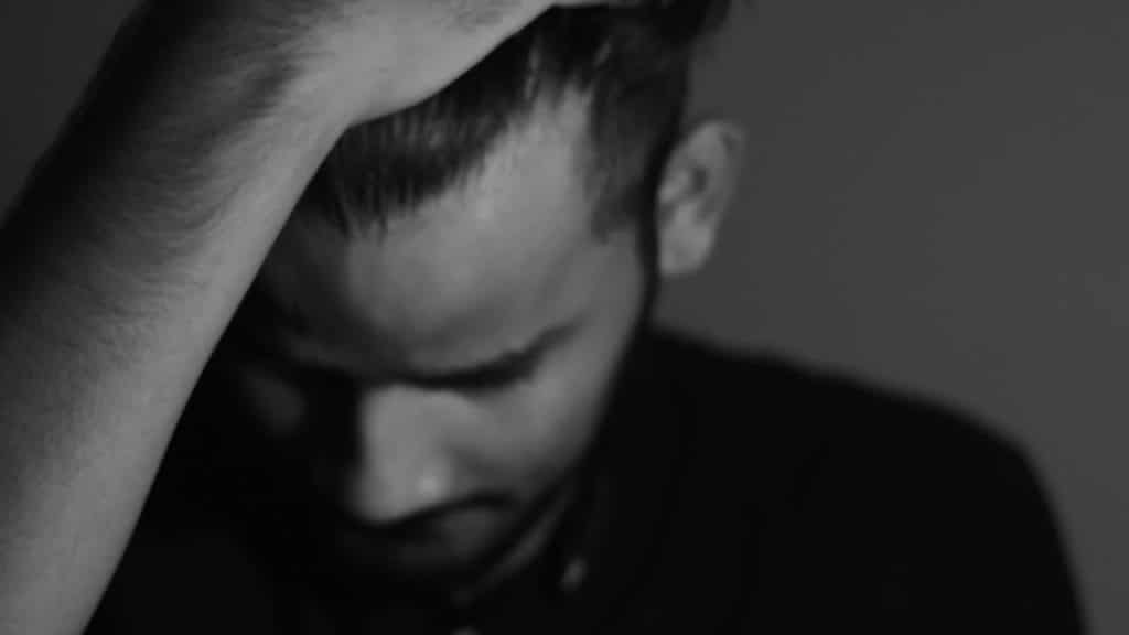 A black-and-white portrait of a man holding his head in distress.