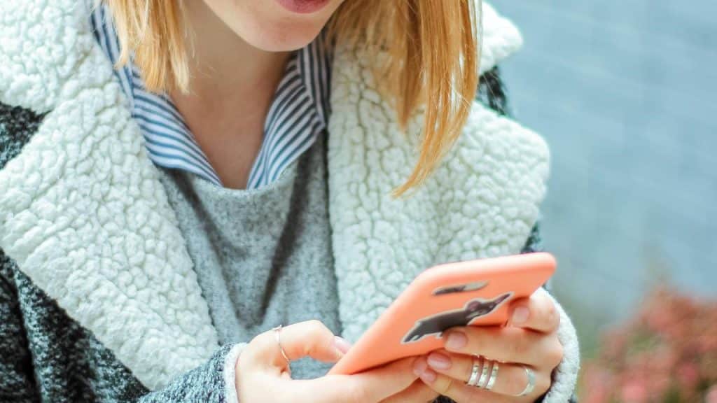 A woman holding a smartphone and looking down at the screen outdoors.