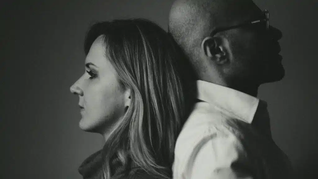 A man and a woman in profile stand back-to-back in a black and white photograph.