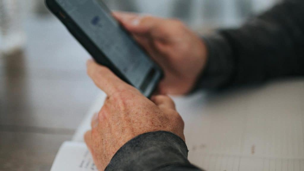 A person holds a smartphone while reading or typing at a desk.