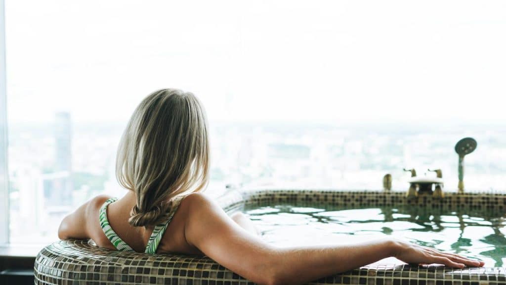 A woman relaxing in a bathtub while looking out over a city view.