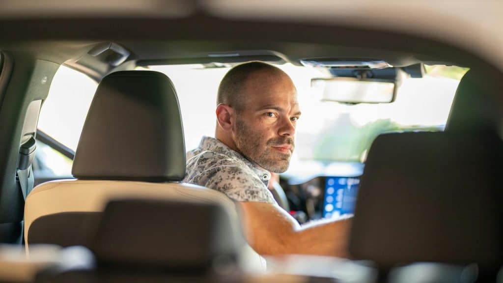 A man sitting in the driver’s seat of a car, looking back over his shoulder.