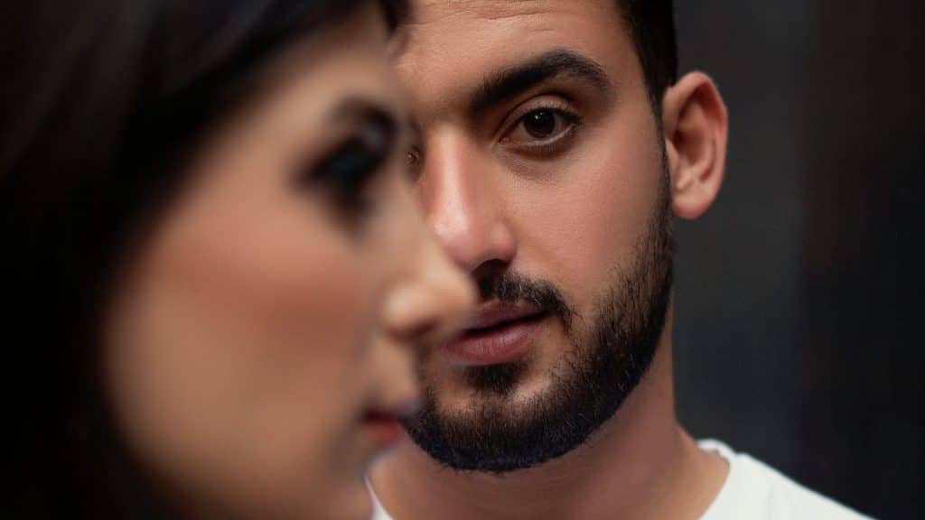 A close-up shot of a man's face partially obscured by the profile of a woman's face.