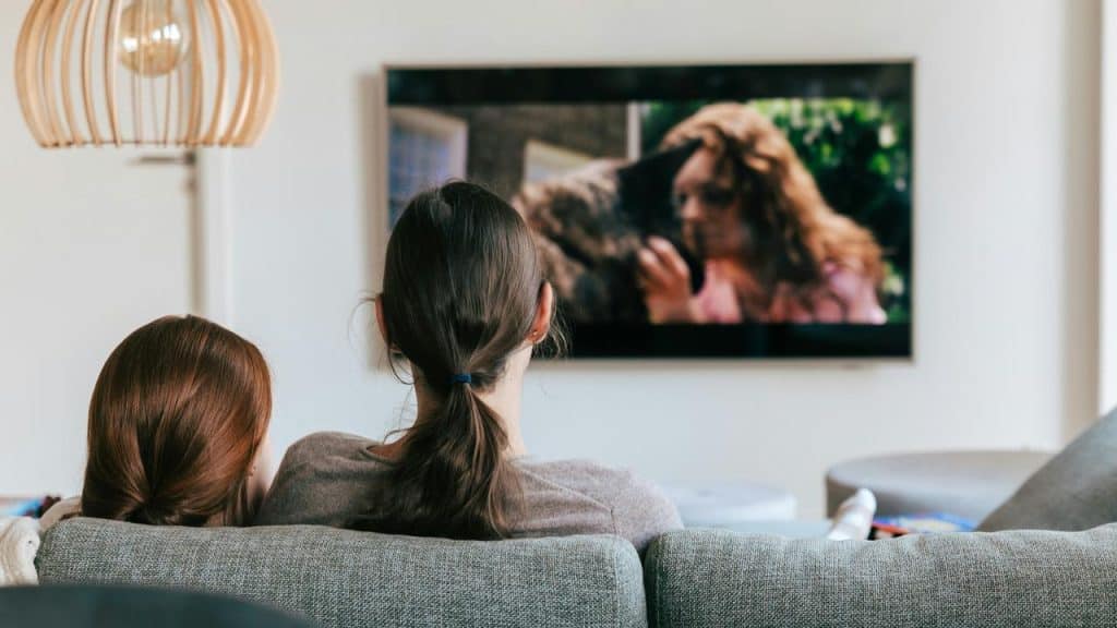 A parent and child sitting on a couch watching television.