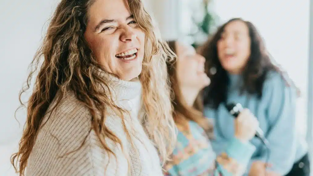 A woman laughing joyfully with friends in a bright indoor setting.