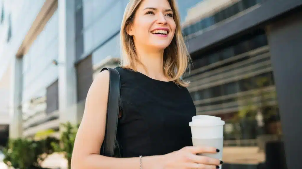 A smiling woman holding a coffee cup while standing outdoors.