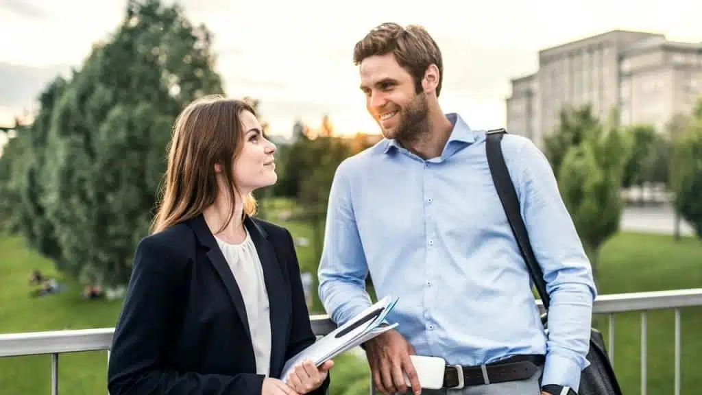 A woman holding documents talking with a man carrying a bag outdoors.