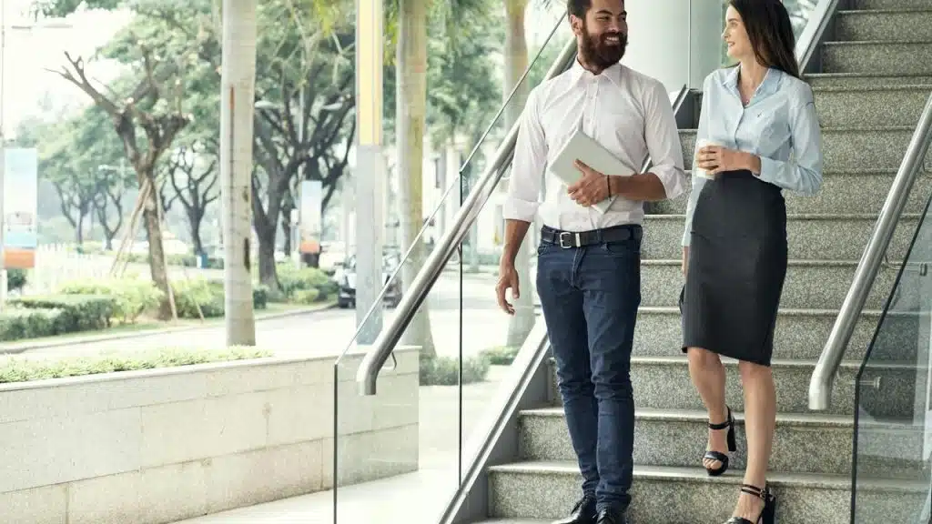A man holding a tablet walking downstairs beside a woman holding a coffee cup.