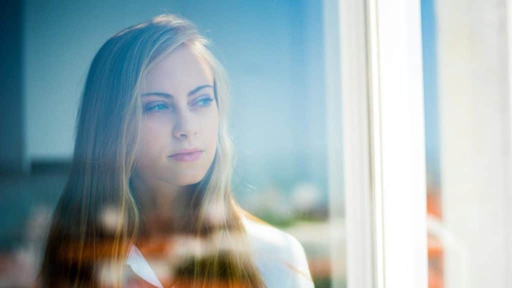 A woman gazing out a window with a distant look.