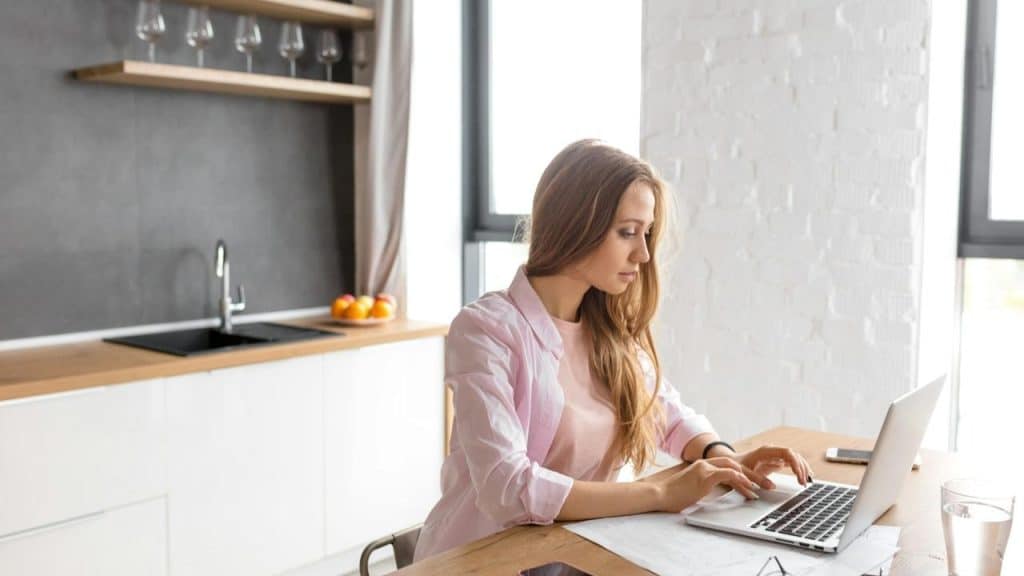 A woman working on a laptop at a kitchen table.