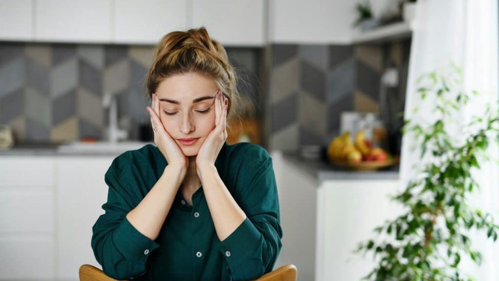 A woman sitting at a table with her head resting in her hands, looking tired or stressed.