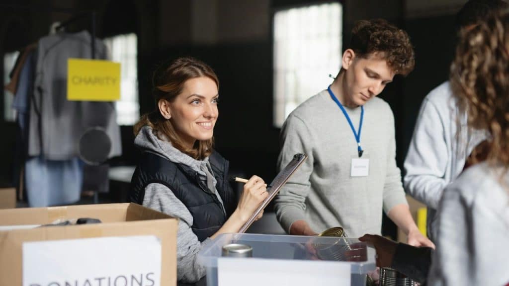 A woman with a clipboard and pen smiles while others sort canned goods into bins.