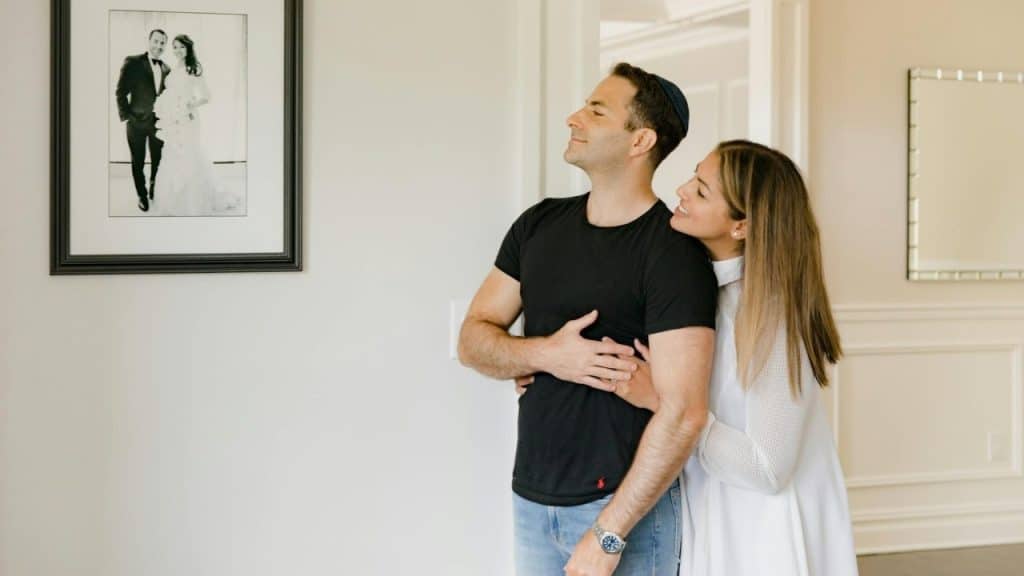 A man and woman stand together looking at a framed black and white wedding photo.