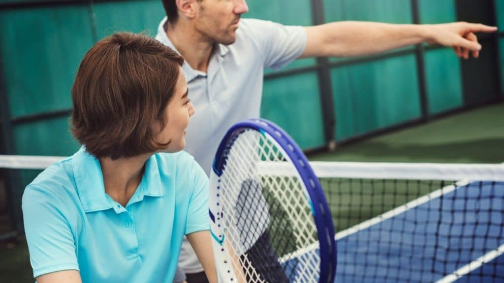 A woman in a blue shirt holds a tennis racket while a man points ahead.