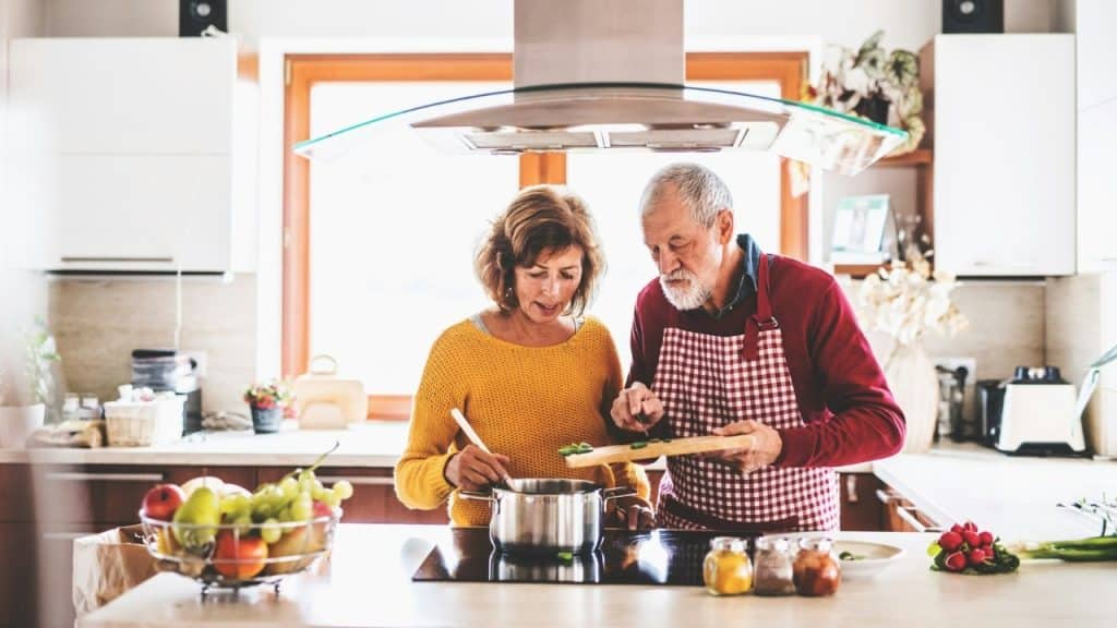 A man in a checkered apron and woman in yellow cook together in a kitchen.